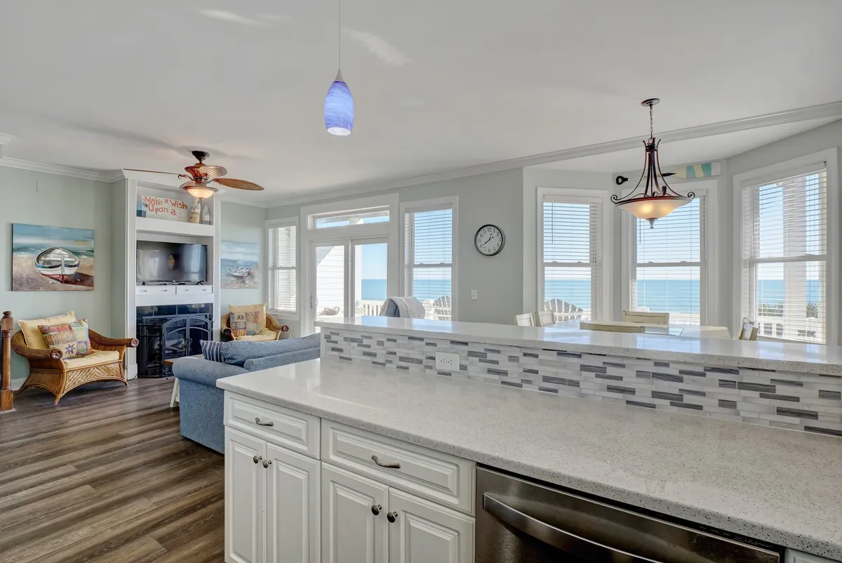 A modern, well-equipped kitchen featuring a spacious countertop, comfortable seating area, large windows overlooking the ocean, and stylish decorative art. The kitchen exudes a casual, welcoming atmosphere that invites group cooking and shared meals.