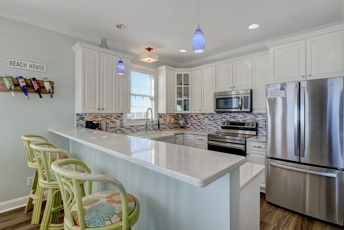 A kitchen with a central island and stools, illuminated by modern light fixtures and adorned with a stylish backsplash. The layout is ideal for both cooking and casual dining, and the scene hints at a relaxed, family-friendly vibe.