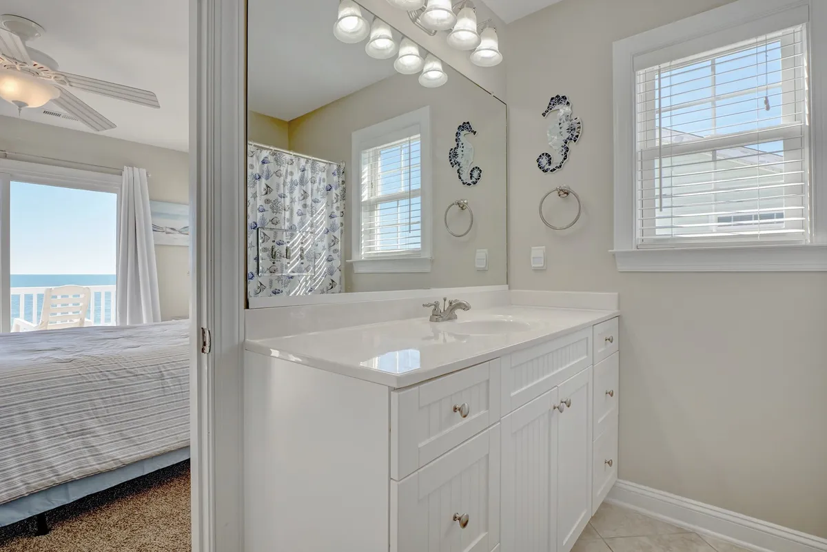 A bathroom featuring a vanity with sink, mirror, modern light fixtures, a shower area, and a window with a view of the ocean. The space feels fresh, bright, and spa-like—ideal for relaxing and rejuvenating.