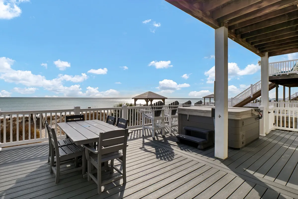 An expansive oceanfront deck equipped with a dining table, bubbling hot tub, and panoramic ocean views. The serene setting is perfect for outdoor dining, unwinding in the hot tub, or socializing with friends and family as the sun sets over the water.
