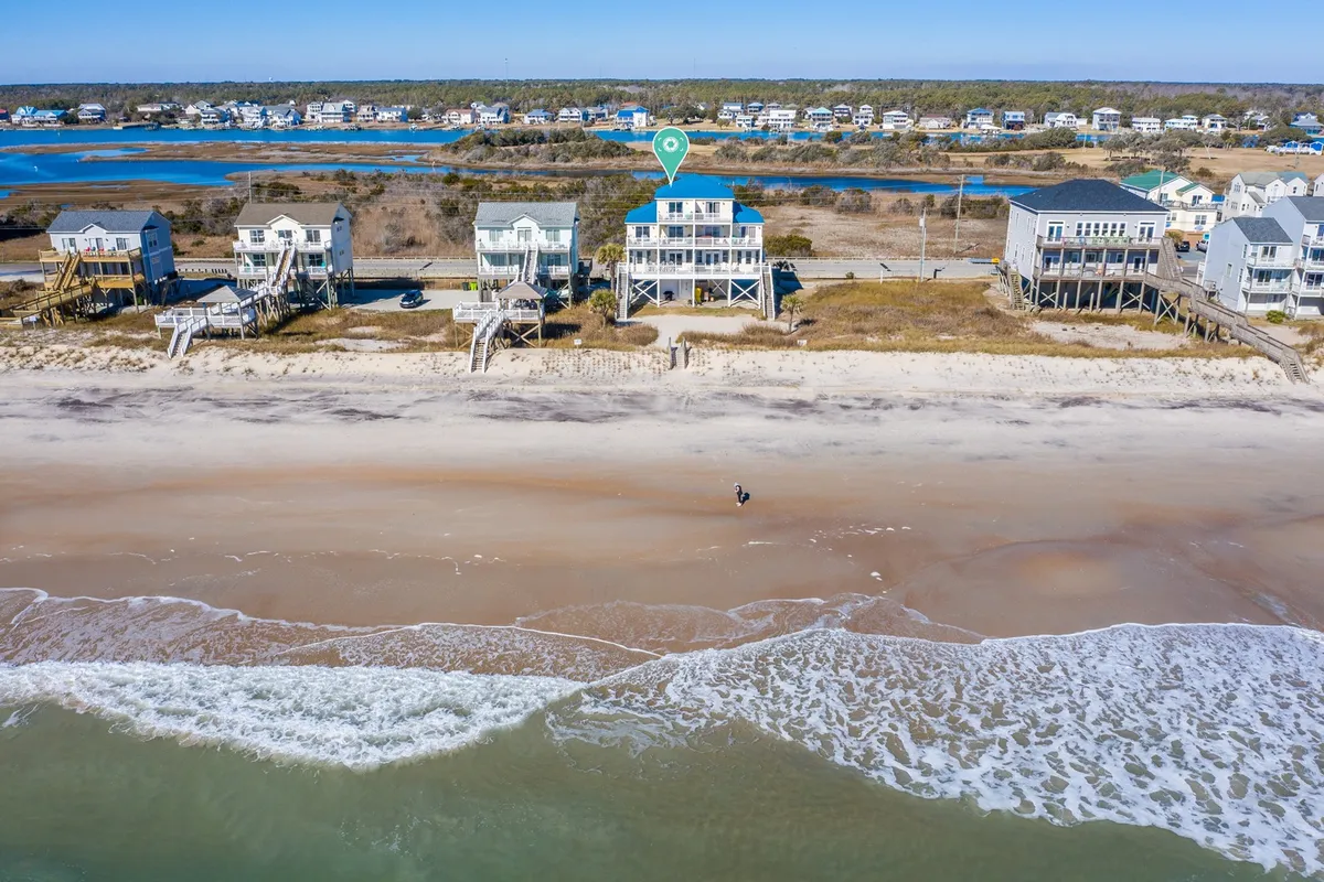 A relaxed exterior shot of a beachfront property with the waves, sandy shore, and distant houses in view. The scene suggests opportunities for family gatherings, water sports, and sun-filled days, highlighting the property’s prime location for seasonal fun.
