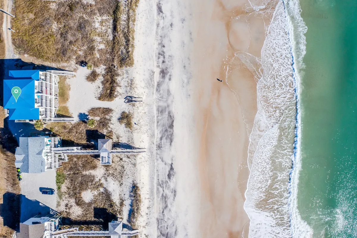 A serene exterior shot of beachfront houses nestled among sand dunes, with gentle waves rolling onto the shore. The image captures the tranquil beauty of Topsail Island and hints at the proximity to outdoor activities like fishing and beach walks.