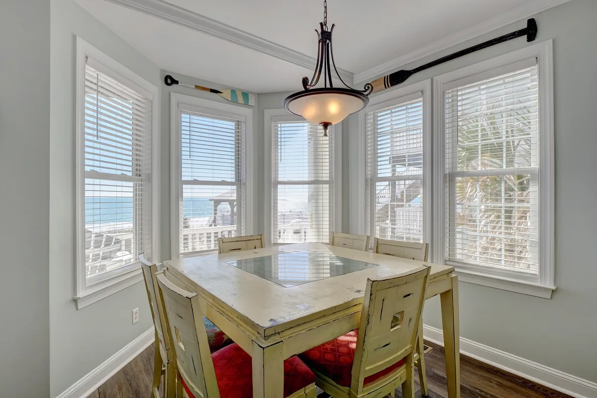A cheerful dining area with a large table under a chandelier, surrounded by expansive windows framing an ocean view. The space feels bright and festive, ideal for family meals, group celebrations, or relaxed coffee mornings.