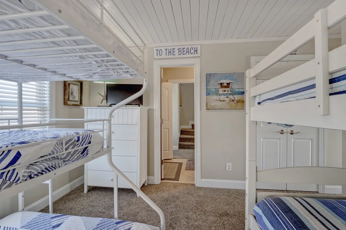 A playful bedroom set up with bunk beds, a 'TO THE BEACH' sign, a dresser, and artwork. The space is bright and relaxed, suitable for children or friends and perfect for sleepovers or family bonding.