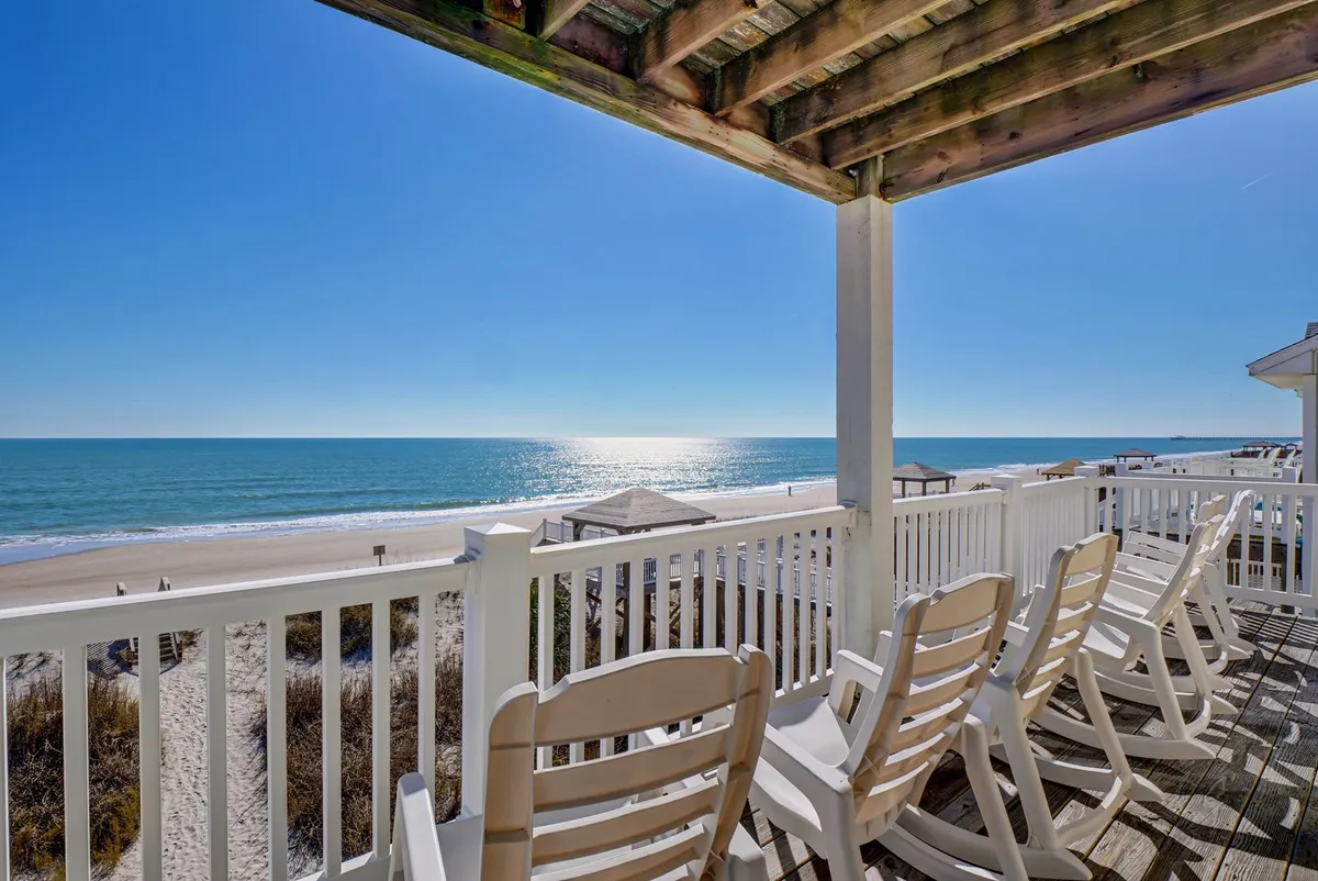 A peaceful exterior shot of a balcony with rocking chairs looking out over the ocean. The image highlights the relaxing atmosphere and the opportunity to enjoy ocean views from an elevated deck, embodying comfort and the home's beachside connection.