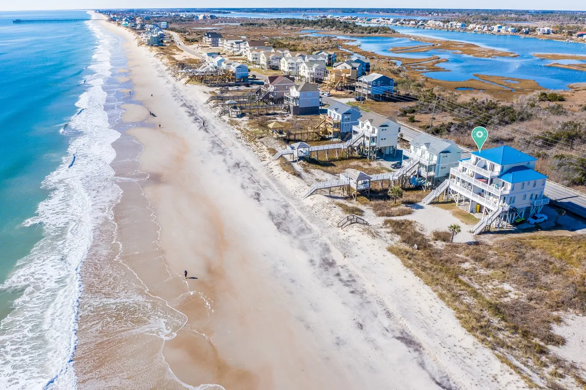 An exterior scene featuring the beach, ocean, and houses with a boardwalk leading towards the shore. The image conveys a welcoming, relaxed mood and showcases easy access to both the beach and local roads—ideal for spontaneous excursions and returning to recharge.