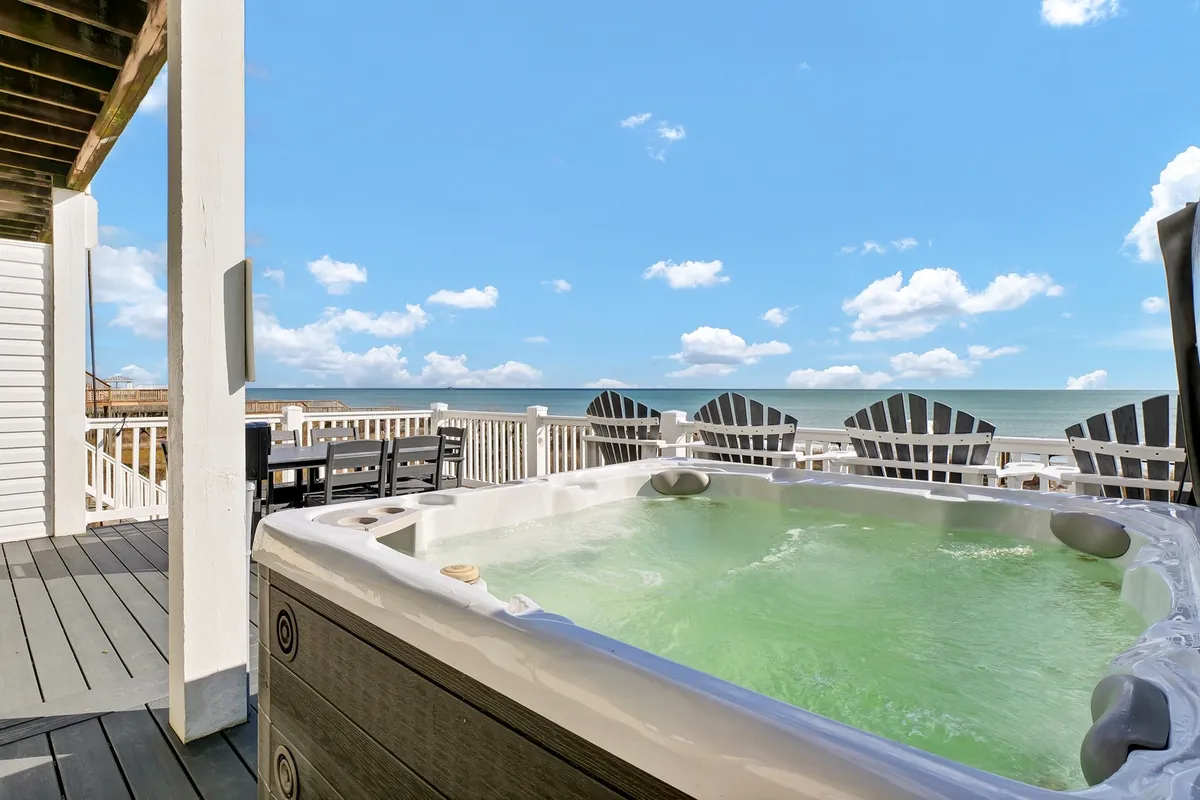 A bubbling hot tub is surrounded by Adirondack chairs on a deck overlooking the rolling waves of the Atlantic. The vantage point allows for panoramic ocean views, ideal for unwinding after a sun-filled day. The peaceful ambiance invites both relaxation and socializing as the sun sets.