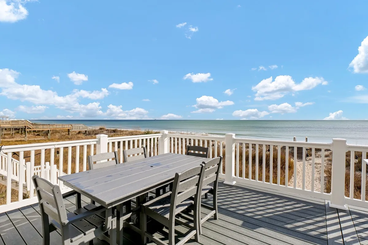 An outdoor dining table set against a backdrop of the ocean and a cloudy sky, inviting guests to dine al fresco while enjoying the sea breeze.